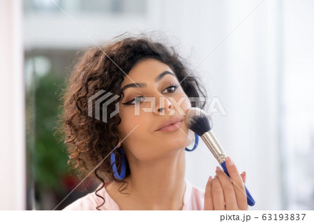 Dark-haired woman applying powder on her face Dark-haired woman applying powder on her face 63193837