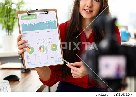 Young woman sitting in office opposite camera and presenting statistics and analytics report. 63199157