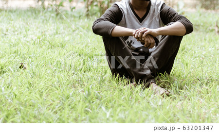 Close up Cropped image of young man in casual clothing sitting over green grass in the park at morning time of day.  63201347