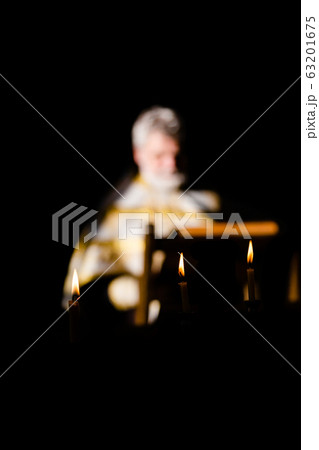Russia, 2020, the Orthodox Church, the priest is out of focus (very blurry), reads a prayer, a prayer book. Three burning candles in the foreground Russia, 2020, the Orthodox Church, the priest is out of focus (very blurry), reads a prayer, a prayer book. Three burning candles in the foreground 63201675