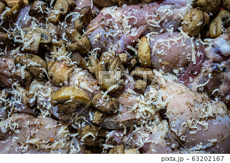 Raw chicken thigh sprinkled with champignons and grated cheese before baking. Close-up Raw chicken thigh sprinkled with champignons and grated cheese before baking. Close-up 63202167