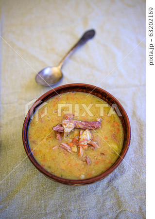 Pea soup with smoked meat, crackers and herbs in a rustic clay plate on a light linen tablecloth 63202169