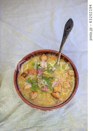 Pea soup with smoked meat, crackers and herbs in a rustic clay plate on a light linen tablecloth Pea soup with smoked meat, crackers and herbs in a rustic clay plate on a light linen tablecloth 63202194