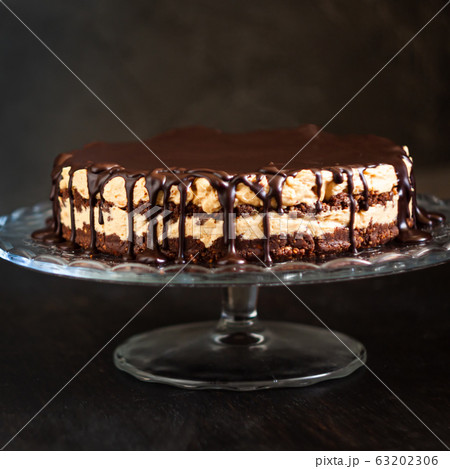 Chocolate round cake layers with butter-cream-nut cream with chocolate drips on a glass stand on a 63202306