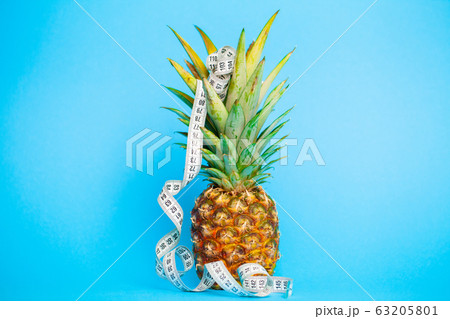 Ripe pineapple with measuring tape on a blue background Ripe pineapple with measuring tape on a blue background 63205801