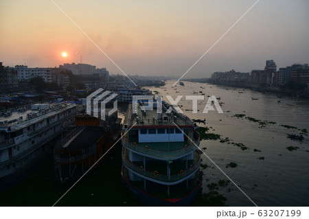 バングラデシュのダッカ　美しい朝日と古い街並み　ブリゴンガ川沿いに停留する客船　川を行き交うボート 63207199
