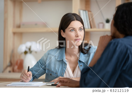 Attentive young female company employee listening to african american client. 63212119