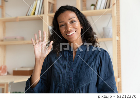 Pleasant smiling biracial woman making hello gesture, looking at camera. 63212270