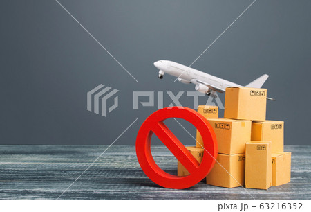 Cardboard boxes near a prohibition symbol NO and freight plane. Restrictions ban on import goods. Sanctions, trade embargo. Isolation quarantine. Manufacturers production slowdown. Flight cancellation 63216352
