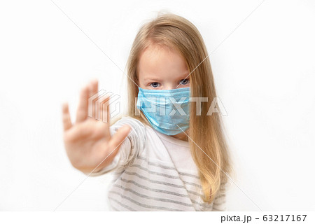 little girl putting up her hand, to say no, or stop, with a serious frowned expression in a medical mask on his face on a light background, close-up. little girl putting up her hand, to say no, or stop, with a serious frowned expression in a medical mask on his face on a light background, close-up. 63217167