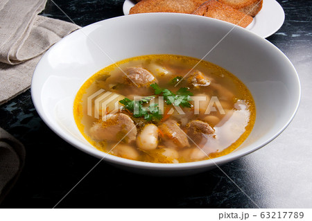 Bean soup in white plate, several toast on white 63217789