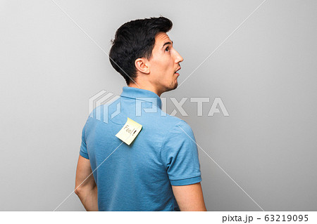 stupid looking man in blue shirt with a yellow sticky note with word fool on his back stupidly looking up 63219095