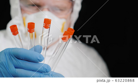 A researcher in a protective suit holds several test tubes 63220868
