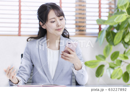 スマホを見ながらスケジュールを確認する若いビジネスウーマン スマホを見ながらスケジュールを確認する若いビジネスウーマン 63227892