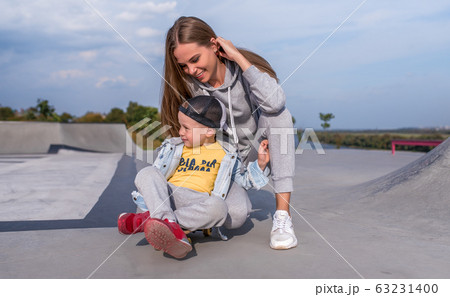 happy family, woman , skates boy son on skateboard, help support in training in sports fitness. Emotions of happiness, fun of relaxation and joy, smile and laughter. Summer sports ground. happy family, woman , skates boy son on skateboard, help support in training in sports fitness. Emotions of happiness, fun of relaxation and joy, smile and laughter. Summer sports ground. 63231400