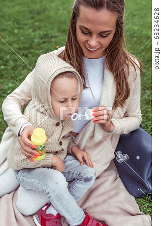 Happy woman mom, little boy plays inflates soap bubbles, casual warm clothes hood. Autumn day summer on grass. Weekend breaks, caring parenting childcare. Emotions Happiness joy fun smile. Happy woman mom, little boy plays inflates soap bubbles, casual warm clothes hood. Autumn day summer on grass. Weekend breaks, caring parenting childcare. Emotions Happiness joy fun smile. 63234628
