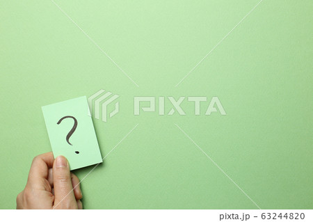 Hand holding question mark memo paper on green background. Solution concept 63244820