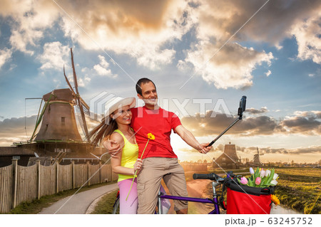 Happy couple on bike against traditional Dutch windmills in Zaanse Schans, Amsterdam area, Holland 63245752