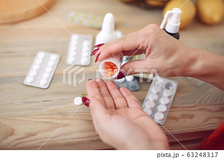 Woman sitting at home with a cold and taking pills Woman sitting at home with a cold and taking pills 63248317