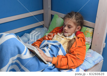 Sick girl reads a book lying in bed in bed Sick girl reads a book lying in bed in bed 63260620