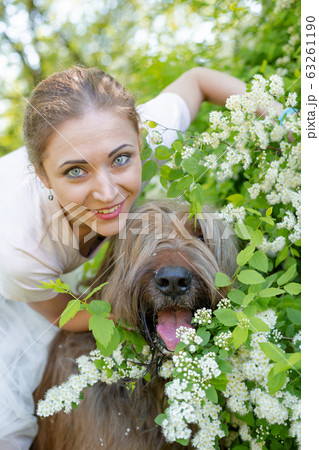 A young girl in a white dress is in the park with her pet dog briard. A young girl in a white dress is in the park with her pet dog briard. 63261190