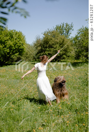A young girl in a white dress is in the park with her pet dog briard. 63261207