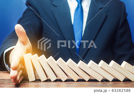 Businessman stops domino falling with his palm. Strategy development. Debt restructuring. Risk management concept. Successful strong business and problem solving. Stop the destructive processes. Businessman stops domino falling with his palm. Strategy development. Debt restructuring. Risk management concept. Successful strong business and problem solving. Stop the destructive processes. 63262586