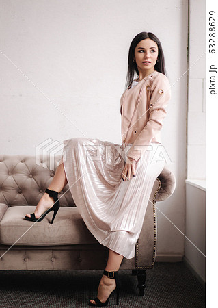 Beautiful brunette woman demonstrating spring clothes in studio. Model sitting on sofa. White background Beautiful brunette woman demonstrating spring clothes in studio. Model sitting on sofa. White background 63288629