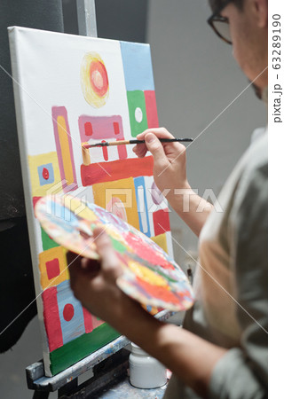 Hand of young artist holding color palette while using paintbrush during work Hand of young artist holding color palette while using paintbrush during work 63289190