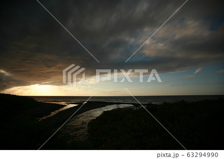 川から海へ、流れ込む湖面に夕日が光る 63294990
