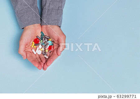 Man's hands holding a lot of different tablets and pills in his hands over blue background Man's hands holding a lot of different tablets and pills in his hands over blue background 63299771