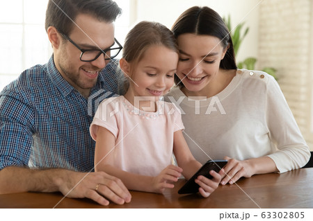 Happy family couple watching funny mobile video with daughter. Happy family couple watching funny mobile video with daughter. 63302805