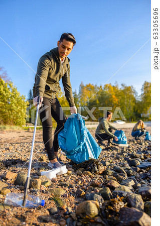 Man cleaning beach with volunteers on sunny day 63305696