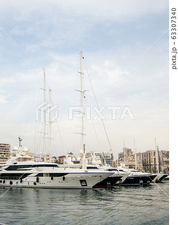 青空の下マヨルカのヨットハーバーに並ぶクルーザーと海岸沿いのリゾートマンション 63307340