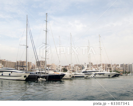 青空の下マヨルカのヨットハーバーに並ぶクルーザーと海岸沿いのリゾートマンション 63307341