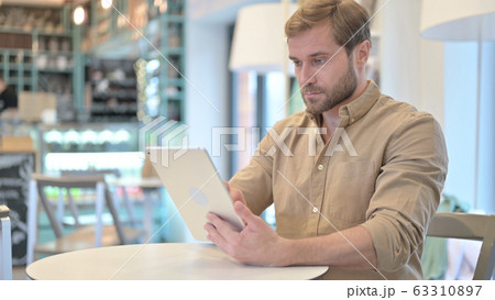 Young Man Using Digital Tablet in Cafe Young Man Using Digital Tablet in Cafe 63310897