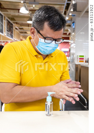 Asian man with face mask apply disinfectant Asian man with face mask apply disinfectant 63311922