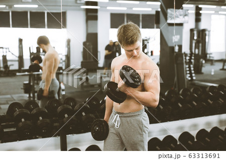Handsome athletic guy bodybuilder, executing exercise with dumbbells, in modern gym 63313691