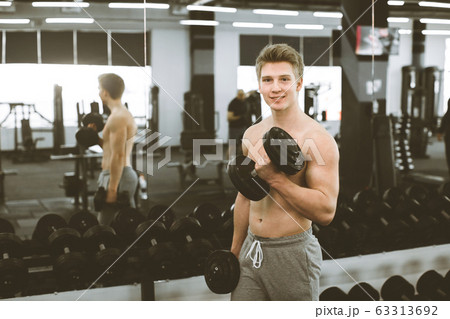 Portrait of young smiling muscular bodybuilder with dumbbells posing in modern fitness gym 63313692