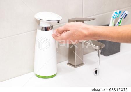 Automatic dispenser of liquid soap in the bathroom close-up. A young guy washes his hands. Automatic dispenser of liquid soap in the bathroom close-up. A young guy washes his hands. 63315052
