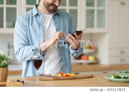 Smiling man using smartphone, cooking salad, preparing vegetables 63317825