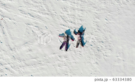 Aerial view from above of children lying on white snow in bright sunshine and making snow angels 63334380