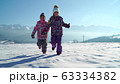 Charming kids in outwear running on snowy terrain with beautiful mountains on background in sunshine 63334382