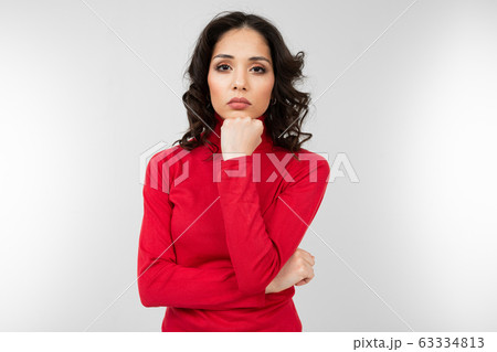 serious brunette girl in a red sweater posing on a white studio background 63334813