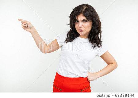 close-up of brunette girl in white t-shirt shows on space with index finger on a white studio 63339144
