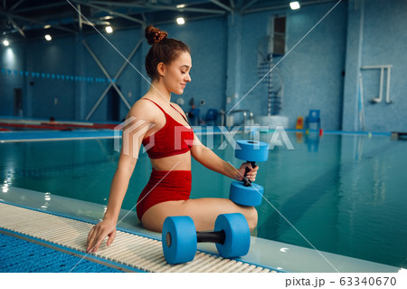 Female swimmer poses at poolside with dumbbells 63340670