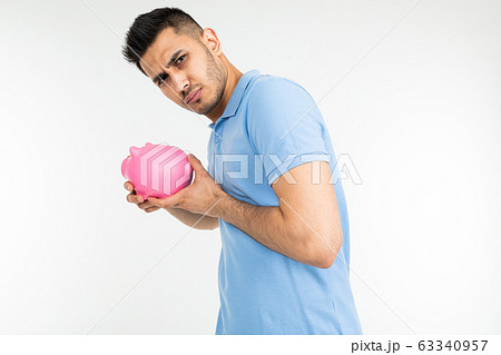 young man in a blue tank holds a piggy bank and refuses on a white studio background 63340957