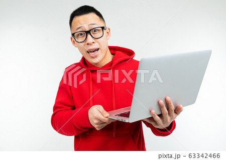 attractive brunette man in casual red hoodie with a laptop in his hands on a white studio background 63342466
