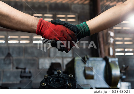 Male and female industrial workers shaking hands in factory workshop wearing protective workwear - Male and female industrial workers shaking hands in factory workshop wearing protective workwear - 63348022