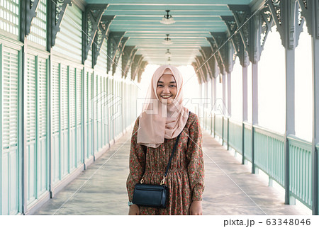 Young and happy Asian muslim girl standing outdoors with bright afternoon sunshine behind her - 63348046